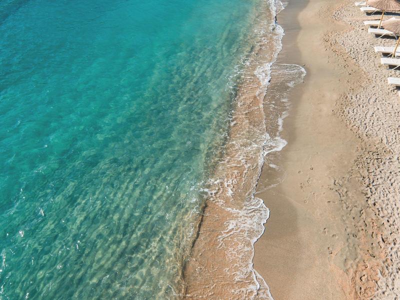 La mer turquoise claire rencontre une large plage de sable avec des vagues et des transats.