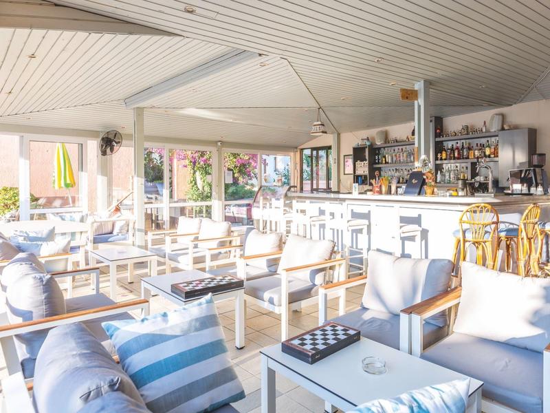Bar de plage lumineuse et ouverte avec mobilier blanc et coussins rayés bleu et blanc.