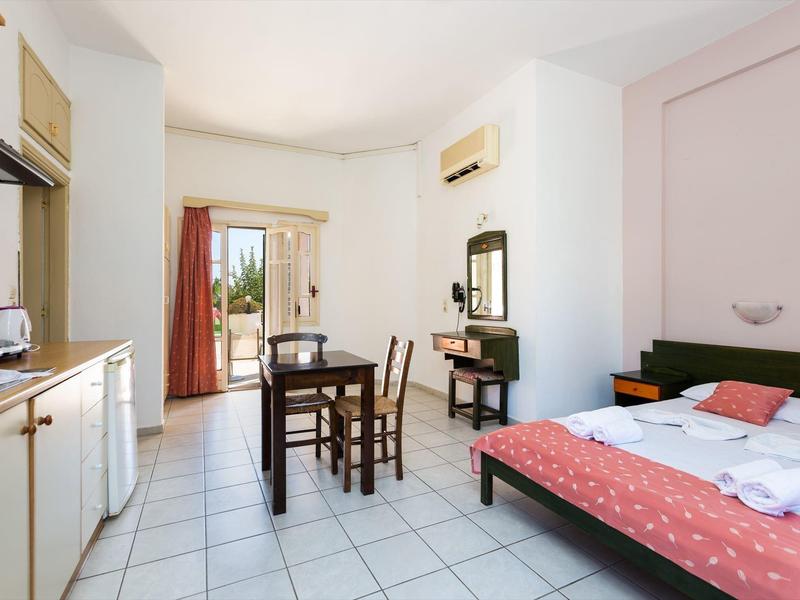 Chambre d'hôtel lumineuse avec lit, table, chaises et kitchenette.