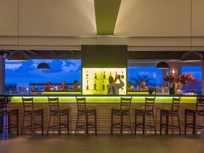 Bar moderna dell'hotel con bancone verde luminoso e vista sul cielo blu.