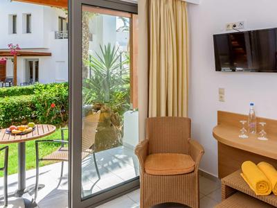 Camera d'hotel luminosa con terrazza, sedie, tavolo e vista sul giardino.