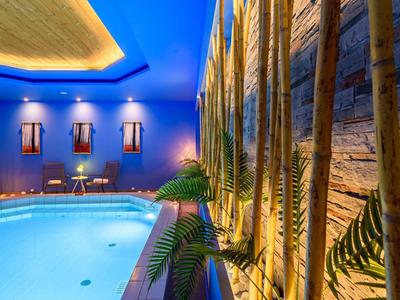 Piscina interna con illuminazione blu e decorazione murale naturale in legno e foglie.