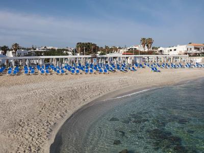 Spiaggia sabbiosa vuota con sedie a sdraio blu e acqua limpida sotto un cielo azzurro.