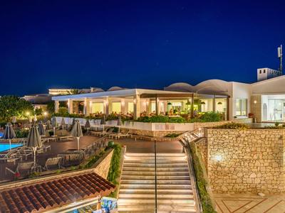 Edificio hotel illuminato con terrazza e piscina di notte sotto un cielo sereno.
