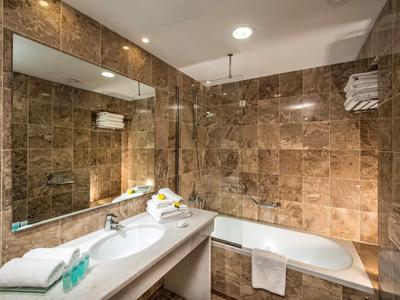 Bagno moderno con pareti in marmo beige, vasca da bagno e grande specchio sopra il lavabo.