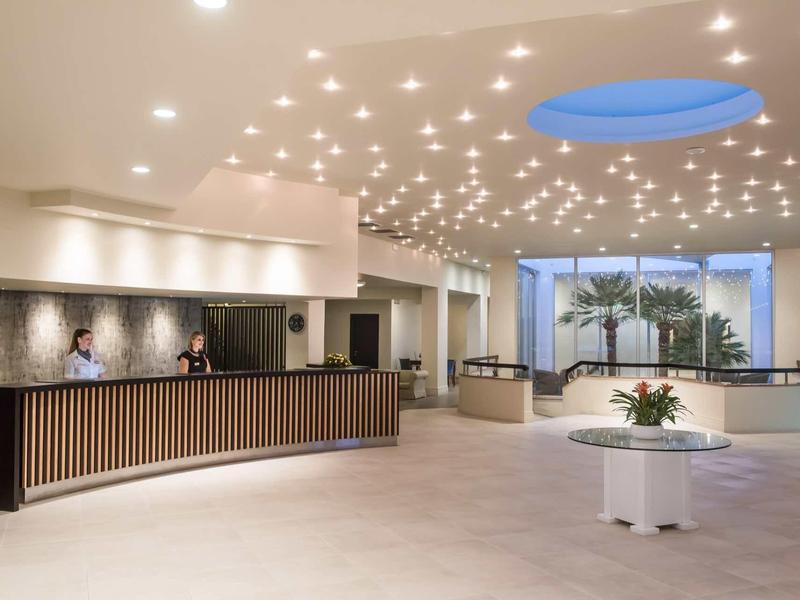 Area reception moderna e luminosa con banco accoglienza e piante.