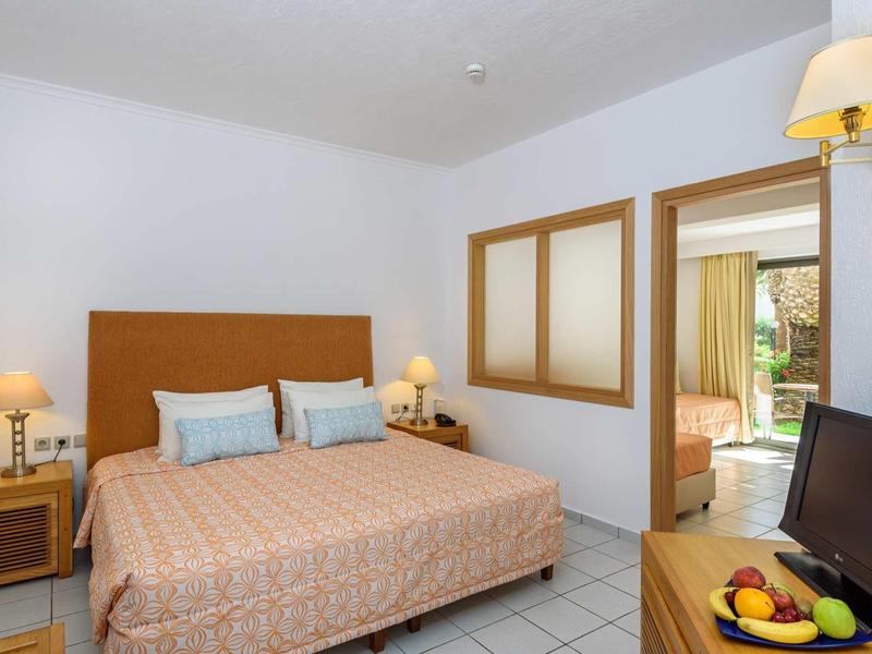 Camera d'hotel luminosa con letto grande, due comodini e TV su scrivania.