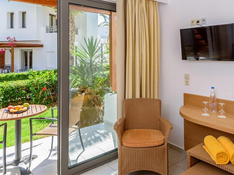 Camera d'hotel luminosa con terrazza, sedie, tavolo e vista sul giardino.