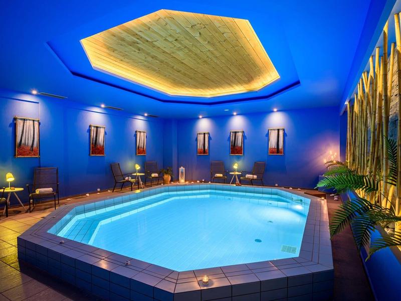 Piscina interna riscaldata in area benessere moderna con illuminazione blu e posti a sedere.