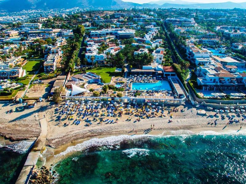 Vista aerea di una spiaggia affollata con hotel e edifici sullo sfondo vicino al mare.
