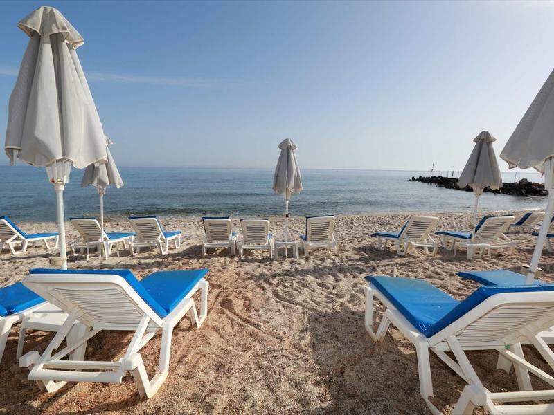 Spiaggia con lettini blu e ombrelloni bianchi sotto un cielo terso vicino al mare.