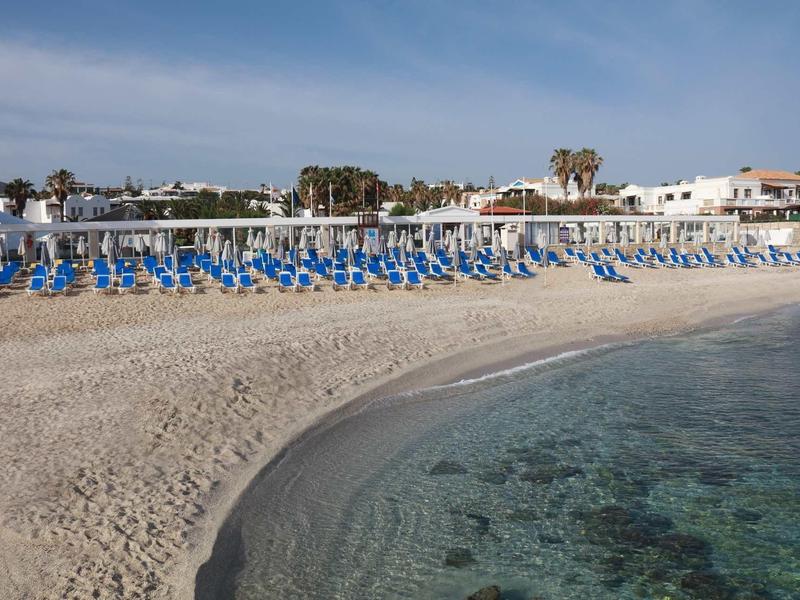 Vista di una spiaggia sabbiosa con lettini blu sotto ombrelloni e acqua limpida.