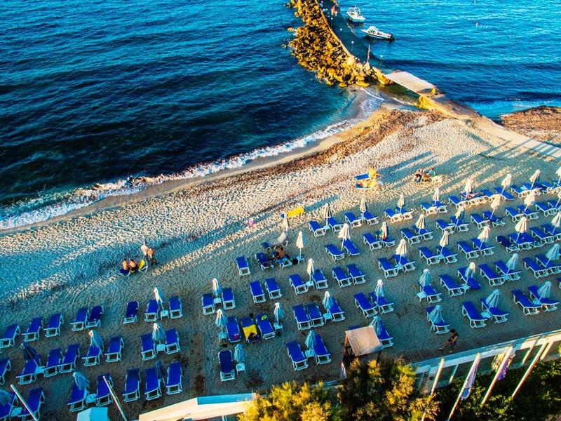 Vista aerea di una spiaggia con lettini blu e ombrelloni gialli vicino al mare.