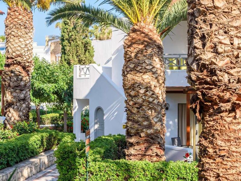 Area dell'hotel con palme e giardino verde ben curato in una giornata di sole.