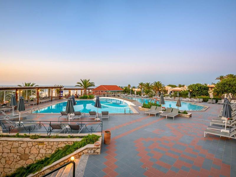 Ampia area piscina all'aperto con lettini, ombrelloni e piante sotto un cielo sereno.