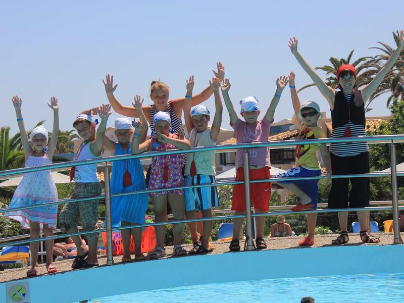 Gruppo di bambini e un adulto su un ponte sopra una piscina con le braccia alzate.
