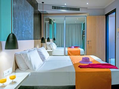 Modernes Hotelzimmer mit großem Bett, orangefarbenem Überwurf und entspannender Beleuchtung.