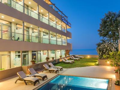 Hotelterrasse mit Pool, Sonnenliegen und Blick auf das Meer bei Dämmerung.