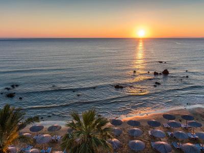 Strand mit Sonnenschirmen, Palmen und Sonnenuntergang über dem ruhigen Meer.