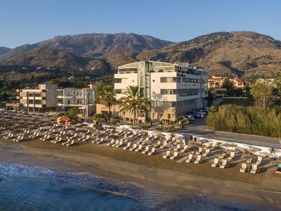 Strandhotel mit Sonnenschirmen und Liegestühlen vor Bergen bei klarem Himmel.