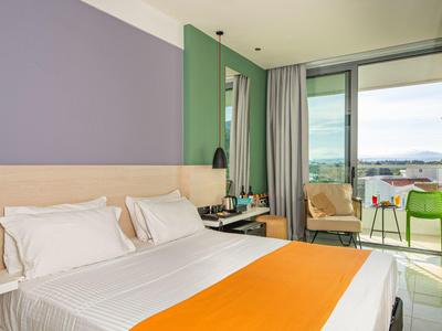 Modernes Hotelzimmer mit Doppelbett, oranger Tagesdecke und Balkon mit Aussicht.