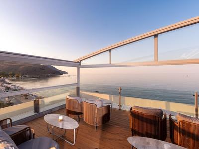 Balcone con area salotto con vista sul mare e una strada costiera al tramonto.