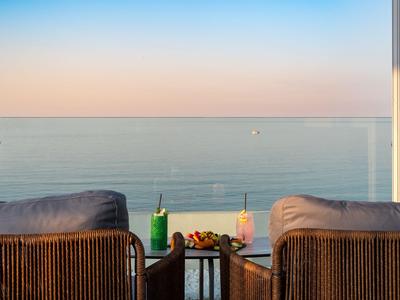 Balcone con sedie e bevande che si affaccia sul mare al tramonto.