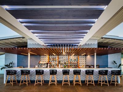 Bar dell'hotel elegante con mobili in legno e una fila di sgabelli davanti a una scaffalatura illuminata.