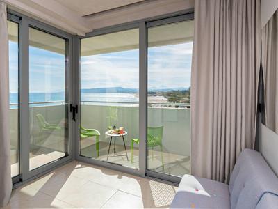 Hotelzimmer mit Balkon, Sitzbereich und Blick auf das Meer bei klarem Himmel.