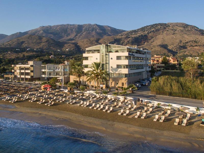Strandhotel mit Sonnenschirmen und Liegestühlen vor Bergen bei klarem Himmel.