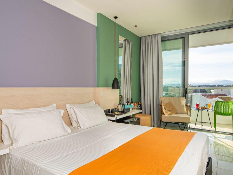 Modernes Hotelzimmer mit Doppelbett, oranger Tagesdecke und Balkon mit Aussicht.