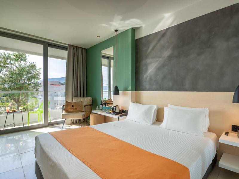 Modernes Hotelzimmer mit Doppelbett, großem Fenster und kleinem Balkon mit Blick ins Grüne.