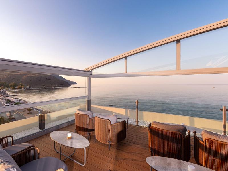 Moderne Terrasse mit Sitzmöbeln und Glasgeländer mit Blick auf das Meer bei Sonnenuntergang.