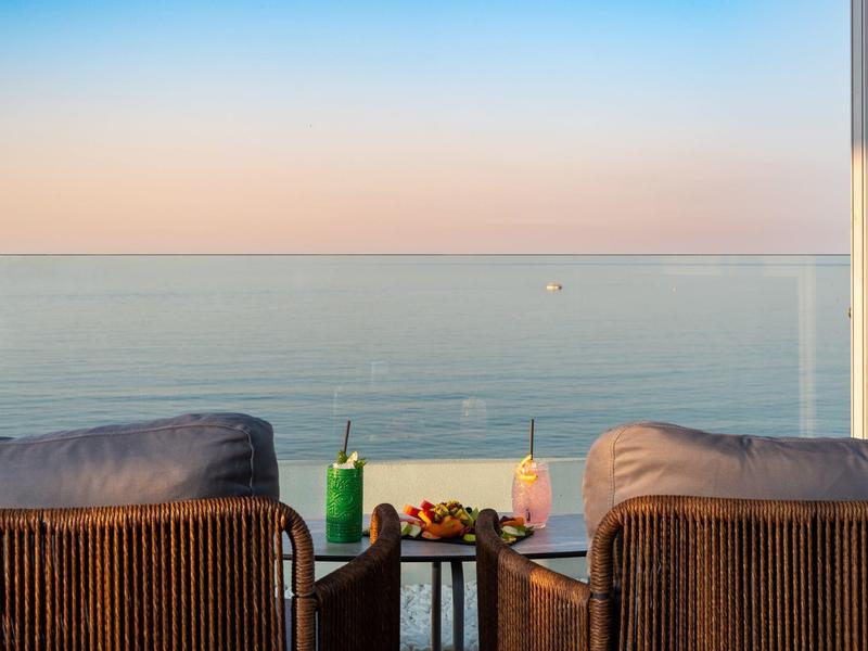 Balkon mit zwei Sesseln, einem kleinen Tisch und Blick auf das Meer bei Sonnenuntergang.