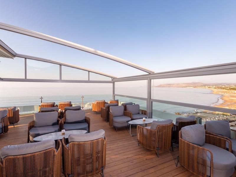 Dachterrasse mit Sitzgelegenheiten und Aussicht auf Meer und Strand bei klarem Himmel.
