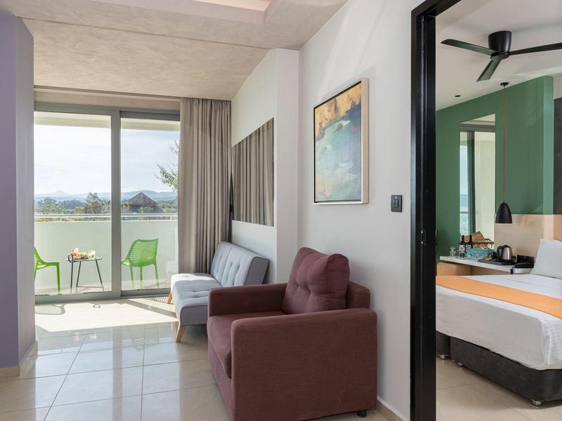 Modernes Hotelzimmer mit Balkon, Sofa und Blick auf grüne Landschaft.
