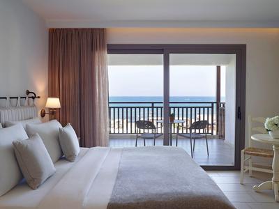 Chambre lumineuse avec grand lit et vue sur la mer et balcon avec chaises.