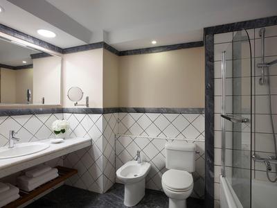 Salle de bain moderne avec toilette, bidet, douche et lavabo sous un miroir éclairé.