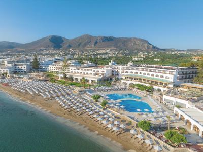 Complexe hôtelier avec piscine, nombreuses chaises longues et accès direct à la plage de sable près des montagnes.
