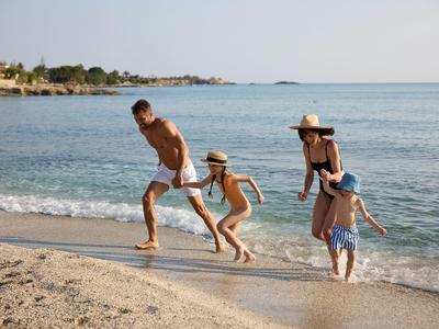 Familie mit zwei Kindern läuft am Strand ins Wasser bei sonnigem Wetter.
