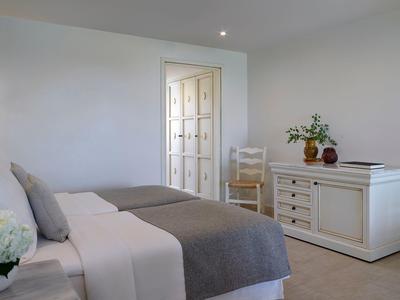 Chambre lumineuse avec lit double, couverture grise et buffet blanc.