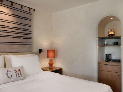 Chambre d'hôtel moderne avec lit blanc, coussin décoratif, lampe de chevet et niche avec étagères.