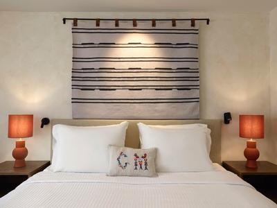 Chambre avec lit blanc, deux oreillers, tapisserie murale au-dessus de la tête de lit et deux tables de chevet avec lampes rouges.