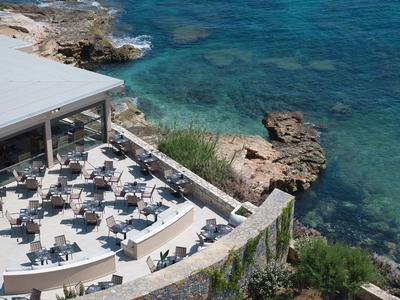 Terrasse eines Restaurants mit Tischen und Stühlen neben klarem blauem Meer und Felsen