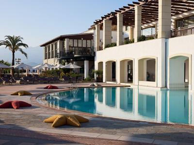 Moderner Hotelpool mit Liegestühlen und Blick auf Berge und Palmen bei Sonnenuntergang.