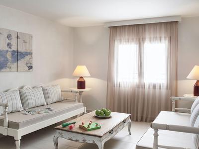 Helles Wohnzimmer mit Sofas, Couchtisch und zwei Lampen neben großen Fenstern mit Vorhängen.