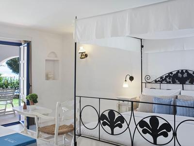 Helles Hotelzimmer mit Doppelbett, Baldachin und Zugang zu einer Terrasse mit Stühlen.