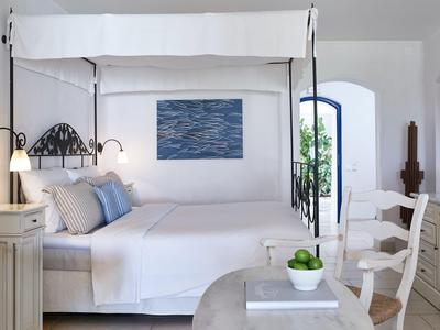 Helles Hotelzimmer mit Doppelbett, weißen und blauen Kissen und Balkon mit Blick ins Grüne.
