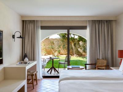 Helles Hotelzimmer mit Doppelbett und Blick auf einen Garten durch eine Glasschiebetür.