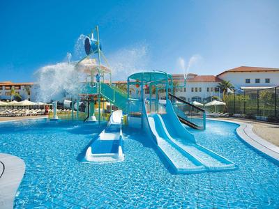 Grand parc aquatique avec toboggans et grands seaux d'eau dans une piscine d'hôtel sous un ciel bleu.